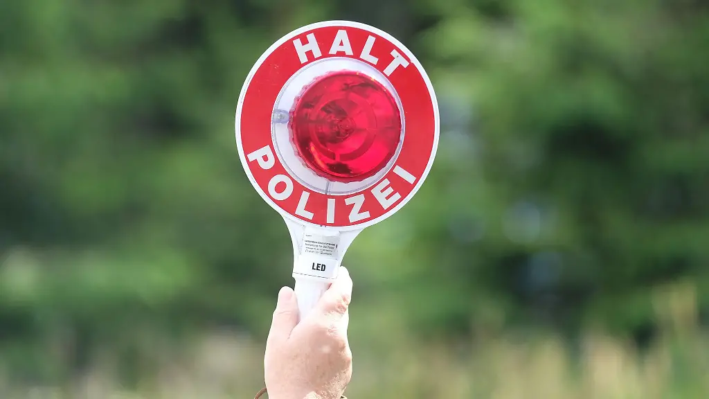 Eine-Polizistin-haelt-waehrend-einer-Polizeikontrolle-eine-rote-Winkerkelle-in-die-Hoehe