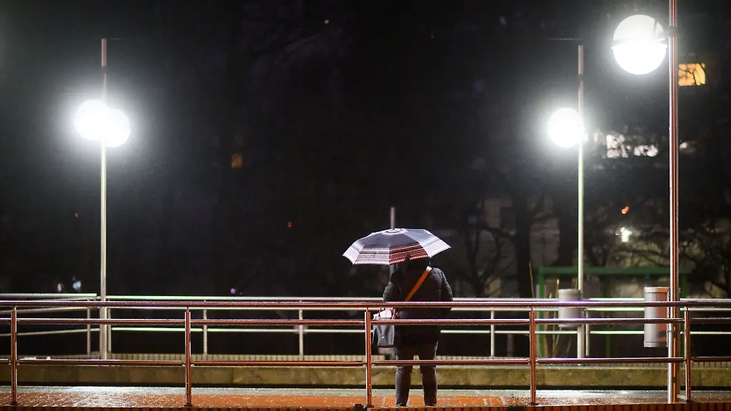 Eine-Frau-wartet-mit-einem-Regenschirm-an-einer-Stadtbahn-Haltestelle