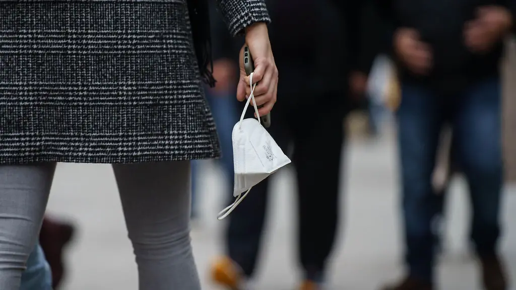 Eine-Frau-traegt-eine-FFP-2-Maske-in-der-Hand