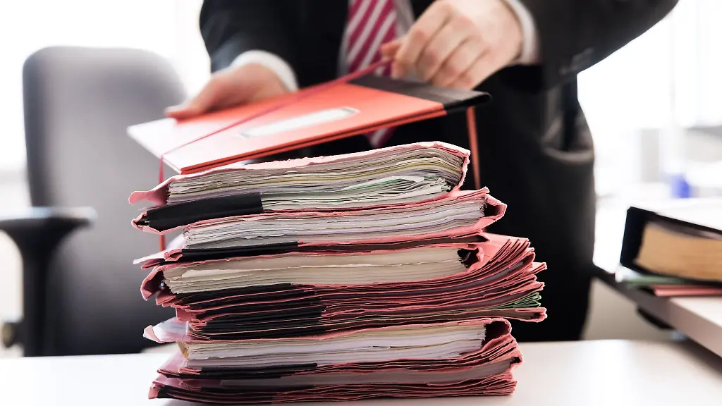 Ein-Staatsanwalt-steht-vor-einem-Stapel-Gerichtsakten