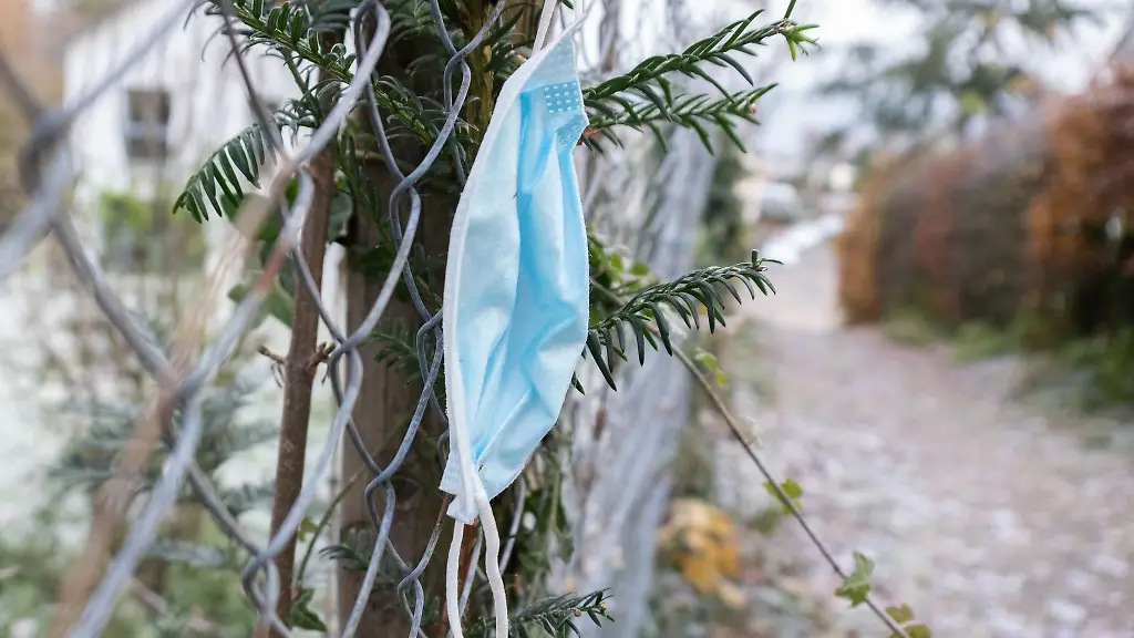 Eine-haengen-gelassene-Maske-ist-an-einem-Zaun-an-einem-Gehweg-zu-sehen