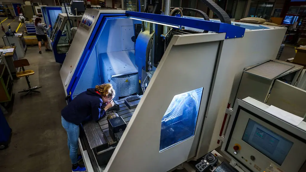 Charlotte-Keilwerth-Schuelerin-steht-an-einer-Maschine-und-prueft-ein-Werkstueck-mit-der-Lupe