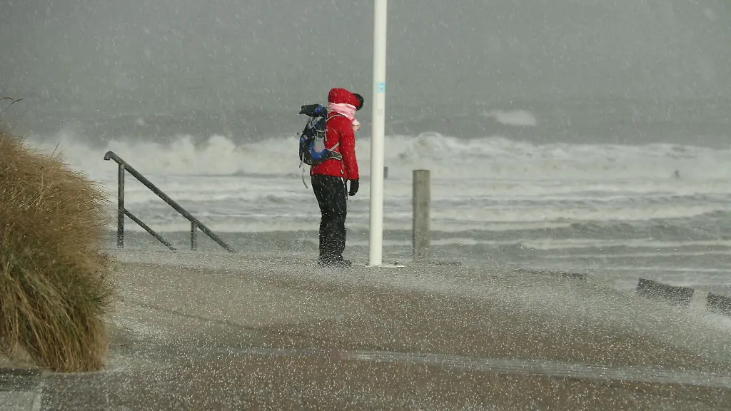 Eine-Spaziergaengerin-blickt-auf-den-Strand-und-die-Wellen-der-vom-Sturm-aufgepeitschten-See