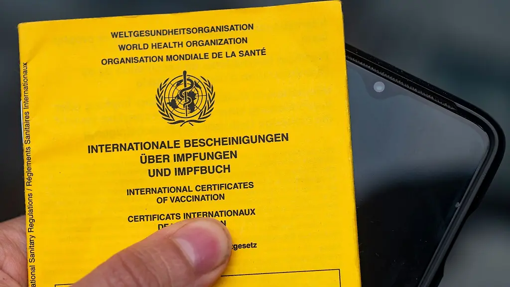 Ein-Smartphone-wird-neben-einem-Impfbuch-gehalten