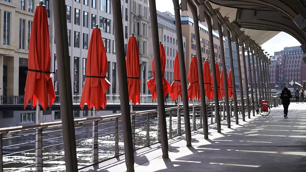 Passanten-gehen-an-dem-leergefegten-Aussenbereich-eines-Cafes-an-den-Alsterarkaden-vorbei