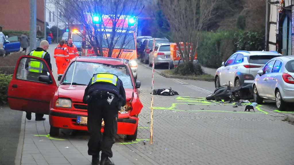 Einsatzkraefte-der-Polizei-und-Feuerwehr-arbeiten-an-der-Unfallstelle-Ein-junger-Rollerfahrer-der-wohl-ohne-Helm-unterwegs-war-ist-bei-einem-Zusammenstoss-mit-einem-Auto-in-Moenchengladbach-lebensgefaehrlich-verletzt-worden