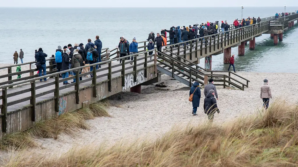 Spaziergaenger-stehen-auf-einer-Seebruecke