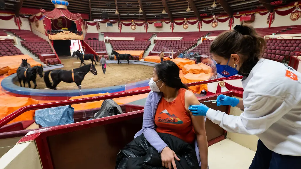 Impfaerztin-Caroline-Klima-r-impft-im-Circus-Krone-Paitul-Supaporn-gegen-das-Corona-Virus-waehrend-im-Hintergrund-Pferde-in-der-Manege-trainieren