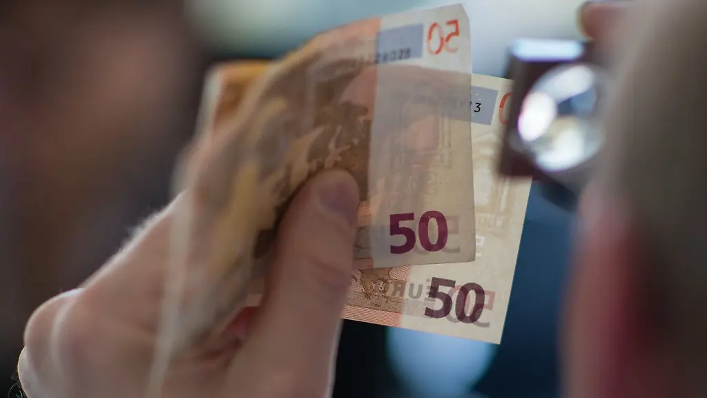 Ein-Mann-prueft-mit-der-Lupe-zwei-50-Euro-Banknoten