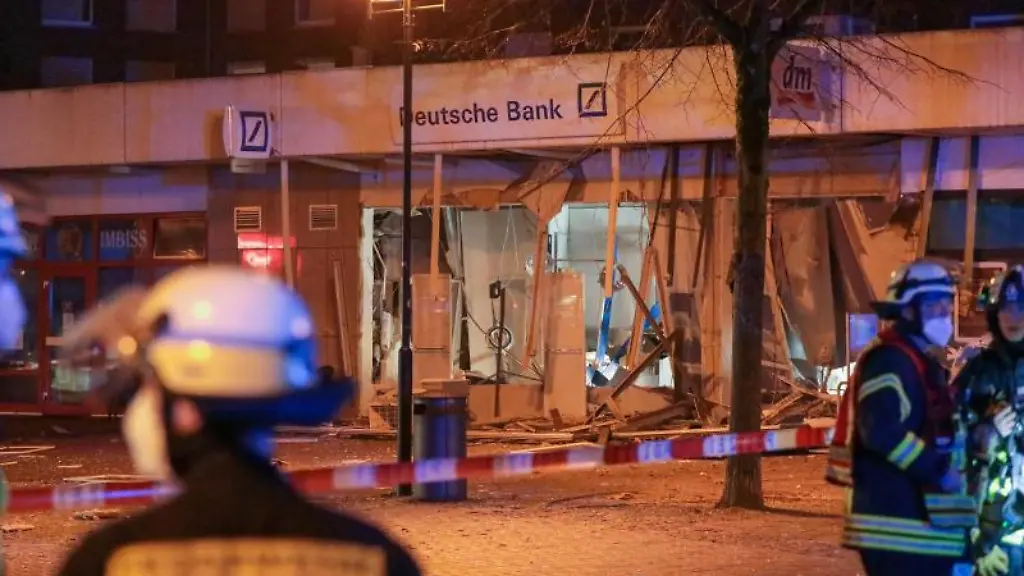 Einsatzkraefte-der-Feuerwehr-stehen-vor-einer-stark-beschaedigten-Deutsche-Bank-Filiale