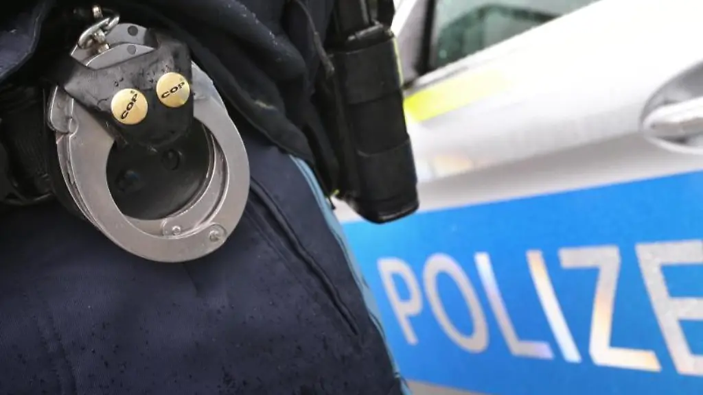 Ein-Polizist-mit-Handschellen-und-einer-Pistole-am-Guertel-steht-vor-einem-Streifenwagen