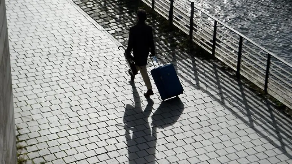 Ein-Mann-geht-mit-seinem-Koffer-am-Spreeufer-entlang