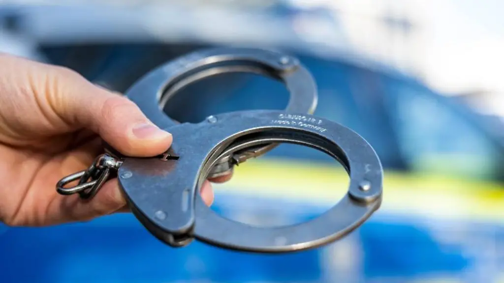 Eine-Hand-haelt-Handschellen-vor-einen-Streifenwagen-der-Polizei
