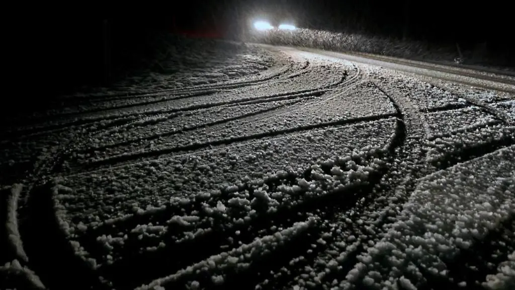Ein-Auto-faehrt-am-fruehen-Morgen-im-Schneetreiben-auf-einer-Strasse