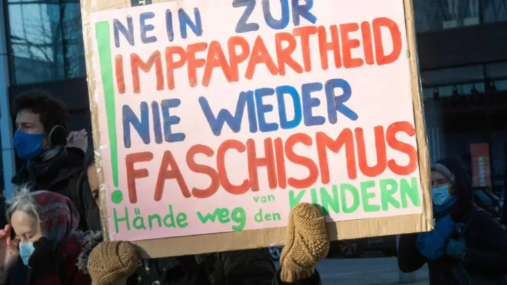 Eine-Teilnehmerin-einer-Demonstration-gegen-die-Impfpflicht-und-Massnahmen-zur-Eindaemmung-der-Coronapandemie-haelt-ein-Plakat-mit-der-Aufschrift-Nein-zur-Impfapartheid-Nie-wieder-Faschismus
