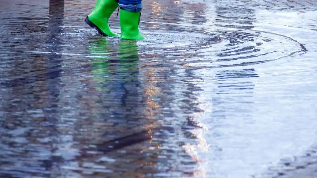 Eine-Passantin-mit-gruenen-Gummistiefeln-geht-durch-eine-Pfuetze