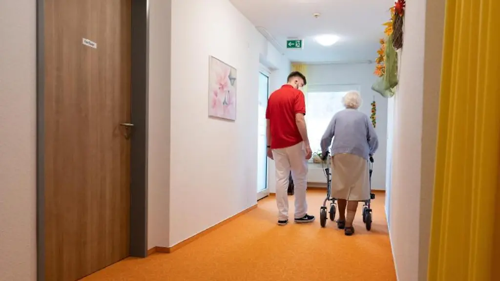 Ein-Betreuer-laeuft-einem-Pflegeheim-mit-einer-Bewohnerin-auf-einem-Flur