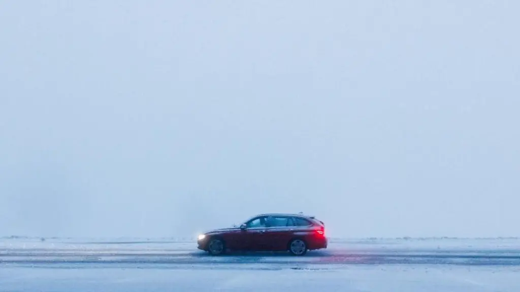 Ein-Auto-faehrt-bei-Nebel-ueber-eine-verschneite-Strasse