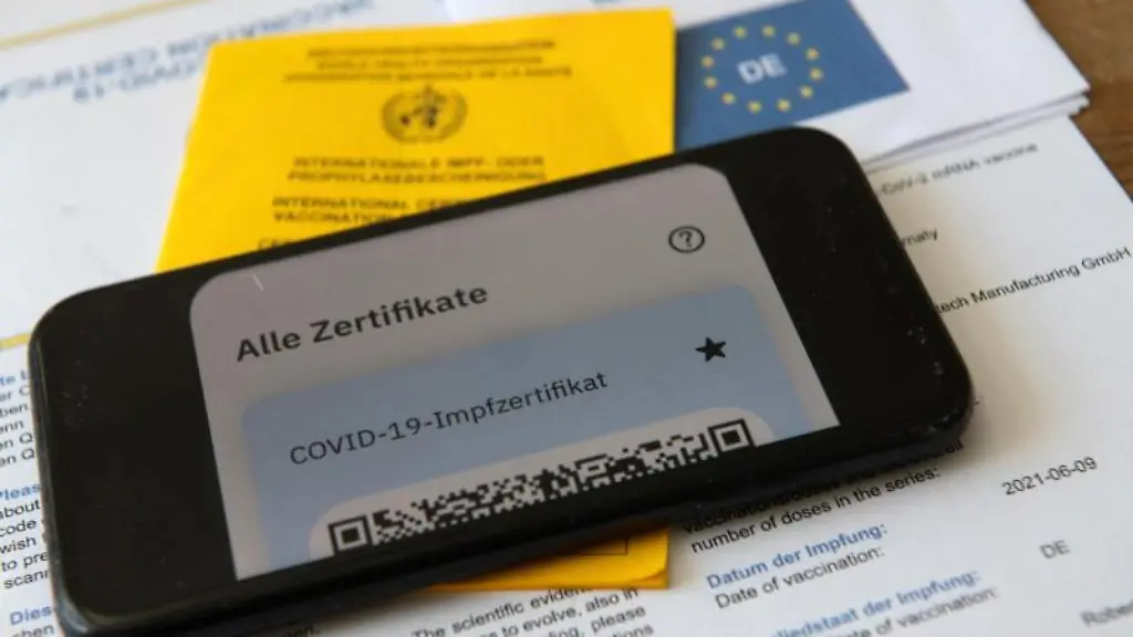 Ein-Impfpass-und-ein-Smartphone-auf-dem-die-App-CovPass-laeuft