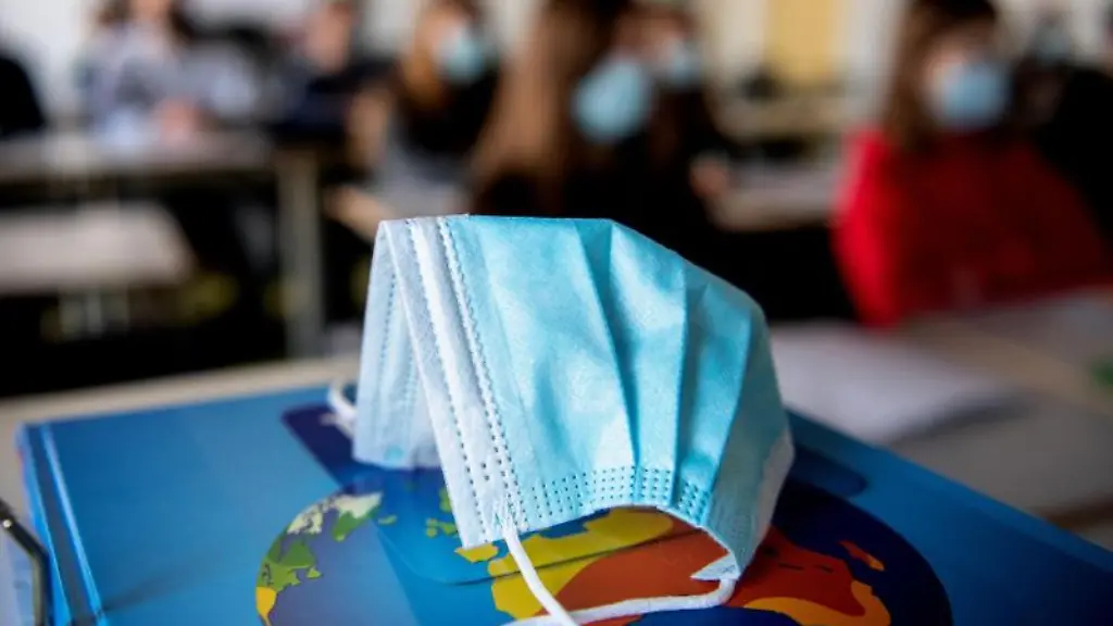 Eine-Maske-liegt-waehrend-einer-Unterrichtsstunde-auf-einem-Buch