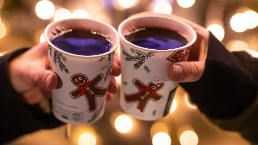 Zwei-Frauen-stossen-mit-Gluehwein-in-Bechern-auf-dem-Weihnachtsmarkt-an