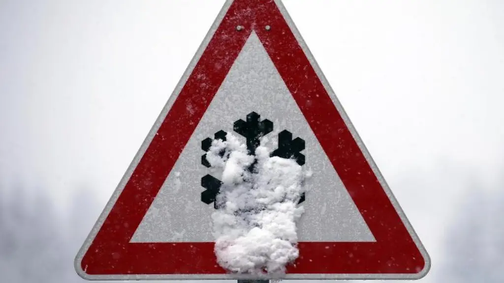 Ein-Verkehrsschild-auf-dem-vor-Schnee-und-Eisglaette-gewarnt-wird-ist-mit-Schnee-bedeckt