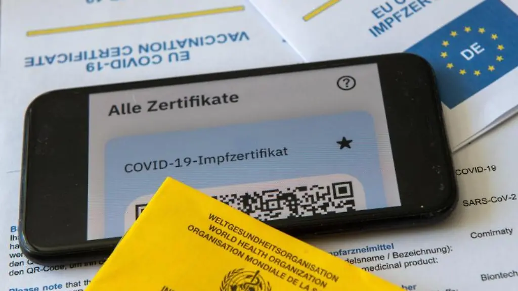 Ein-Impfpass-und-ein-Smartphone-mit-der-CovPass-App-liegen-auf-einem-Impfzertifikat
