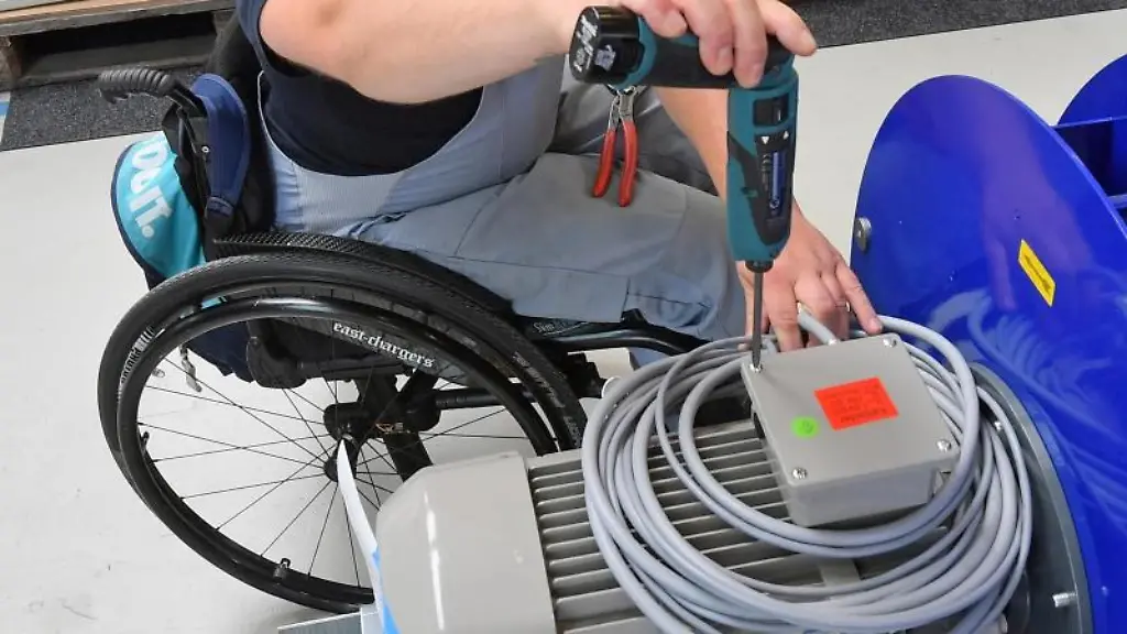 An-einem-Arbeitsplatz-fuer-Motorklemmen-ist-ein-Mitarbeiter-im-Rollstuhl-mit-Montagearbeiten-beschaeftigt