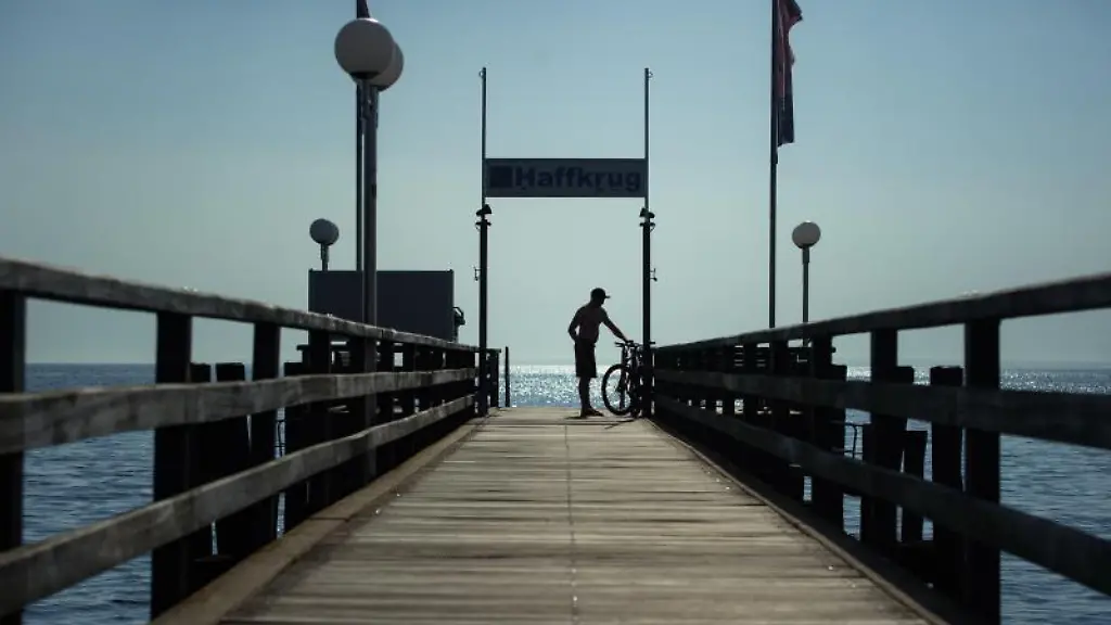 Ein-Besucher-steht-auf-der-Seebruecke-am-Ostseestrand-in-der-Dorfschaft-Haffkrug-der-Gemeinde-Scharbeutz