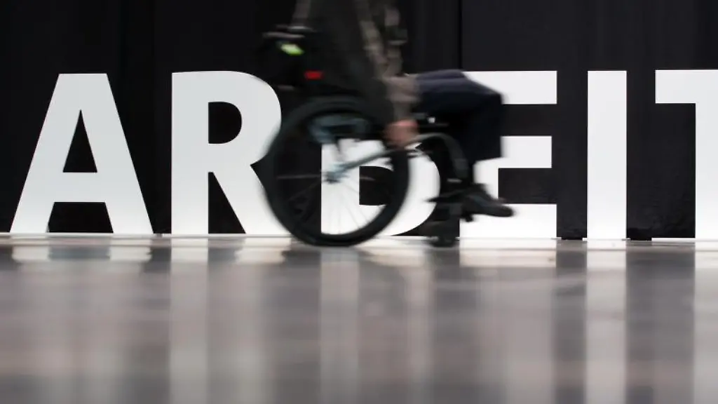 Ein-Mann-faehrt-mit-seinem-Rollstuhl-an-dem-aufgestellten-Wort-Arbeit-entlang