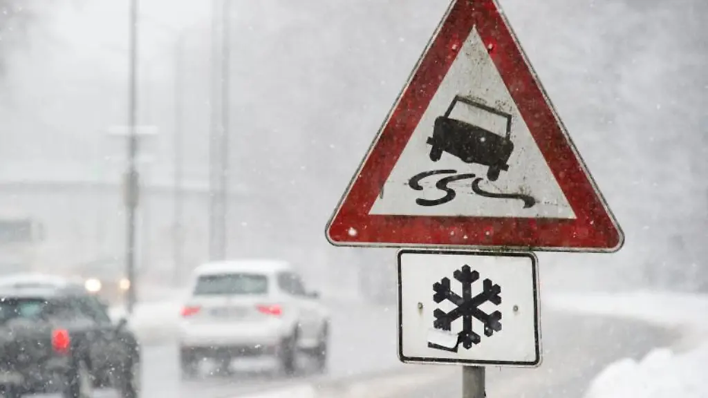 Ein-Warnschild-steht-bei-Schnee-und-Glaette-am-Strassenrand