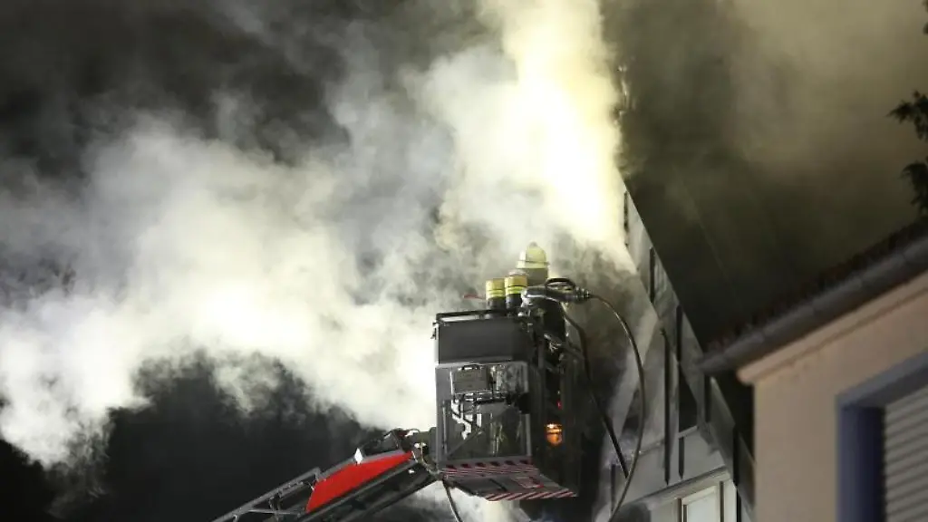 Einsatzkraefte-der-Feuerwehr-loeschen-in-einem-Haus-einen-Zimmerbrand