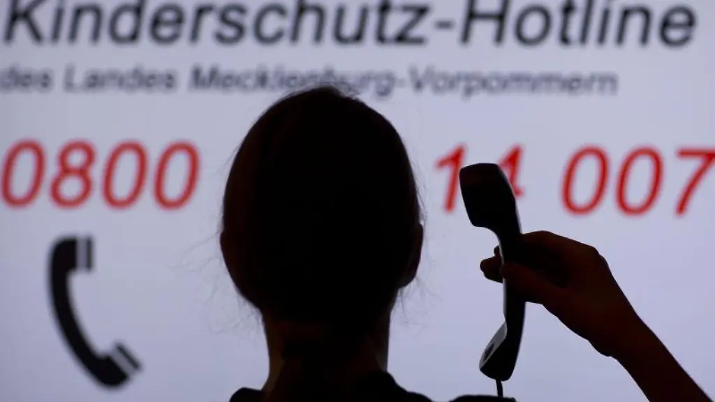 Ein-Maedchen-haelt-einen-Telefonhoerer-vor-einer-Informationstafel-der-Kinderschutz-Hotline