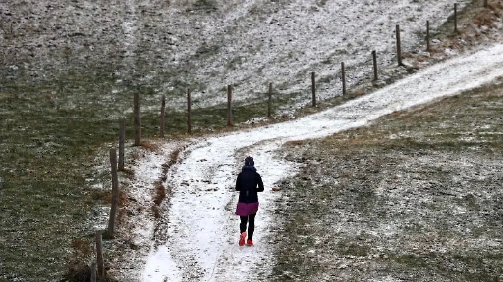 Eine-Frau-joggt-durch-die-mit-einer-duennen-Schneeschicht-ueberzogenen-Landschaft