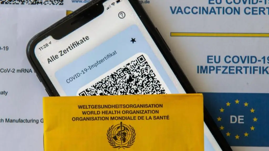 Ein-Impfpass-und-ein-Smartphone-mit-der-CovPass-App-liegen-auf-einem-Impfzertifikat