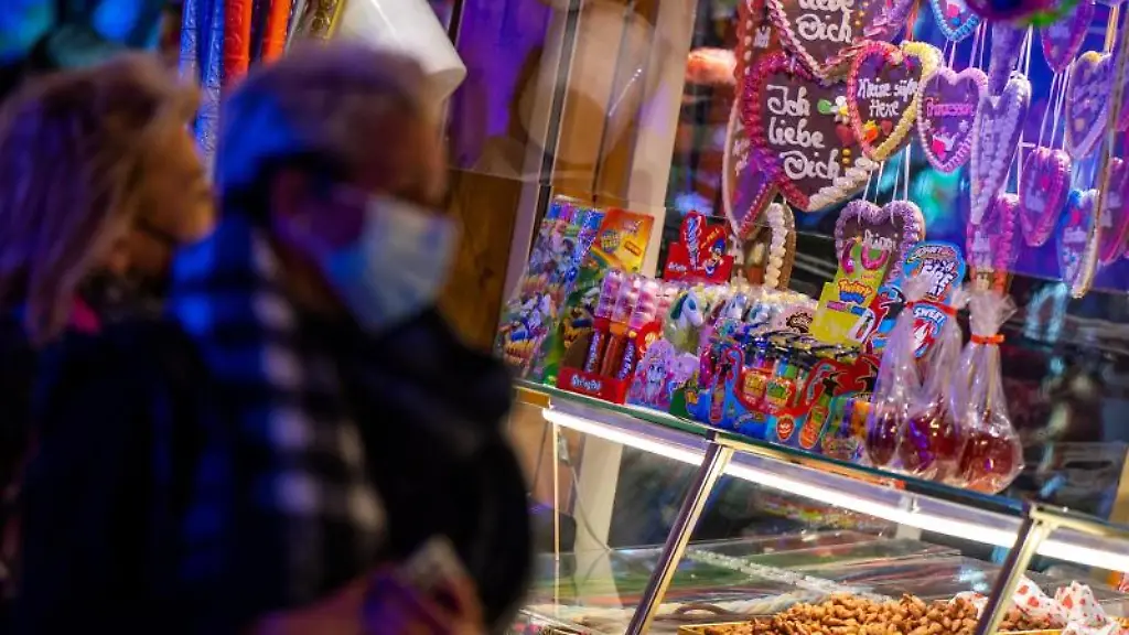 Besucher-eines-Weihnachtsmarktes-stehen-vor-einem-Suessigkeitenstand