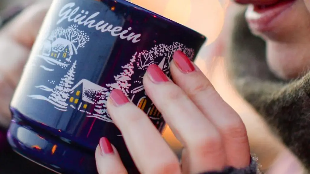 Eine-Frau-haelt-auf-einem-Weihnachtsmarkt-eine-Tasse-mit-Gluehwein-in-den-Haenden