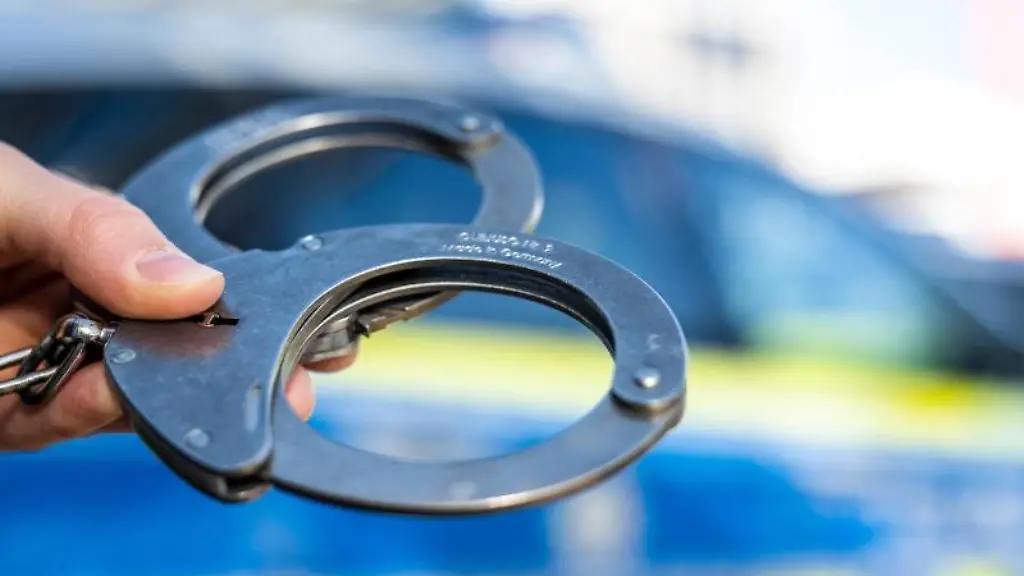 Eine-Hand-haelt-Handschellen-vor-einen-Streifenwagen-der-Polizei