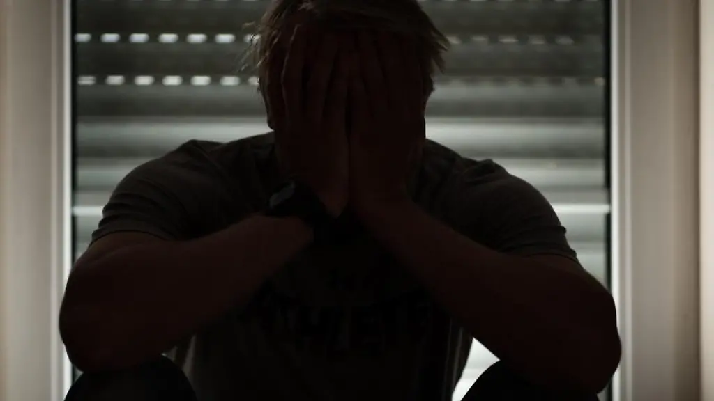 Ein-Mann-sitzt-in-seiner-Wohnung-und-haelt-seine-Haende-vor-sein-Gesicht