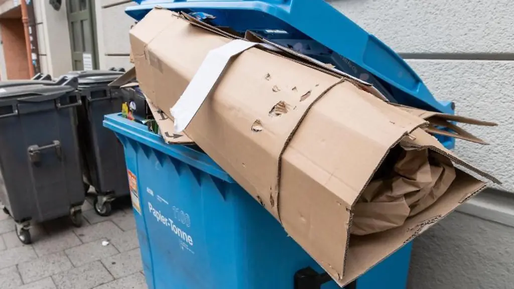 Ein-ueberfuellter-Muellcontainer-fuer-Papier-und-Pappe-steht-am-Tag-der-Entleerung-vor-einem-Haus