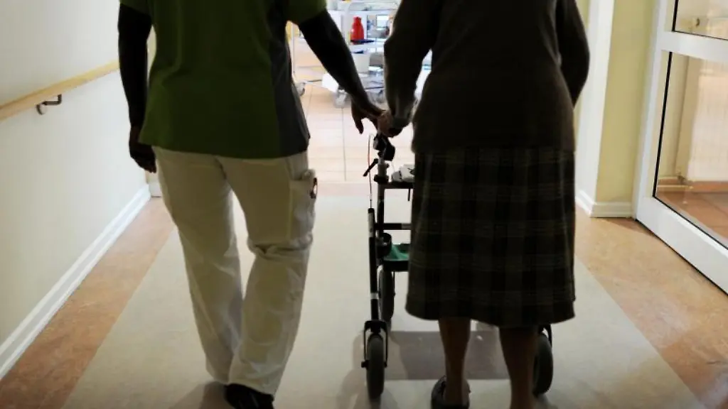 Eine-Bewohnerin-und-eine-Pflegehelferin-gehen-in-einem-Seniorenzentrum-einen-Gang-entlang