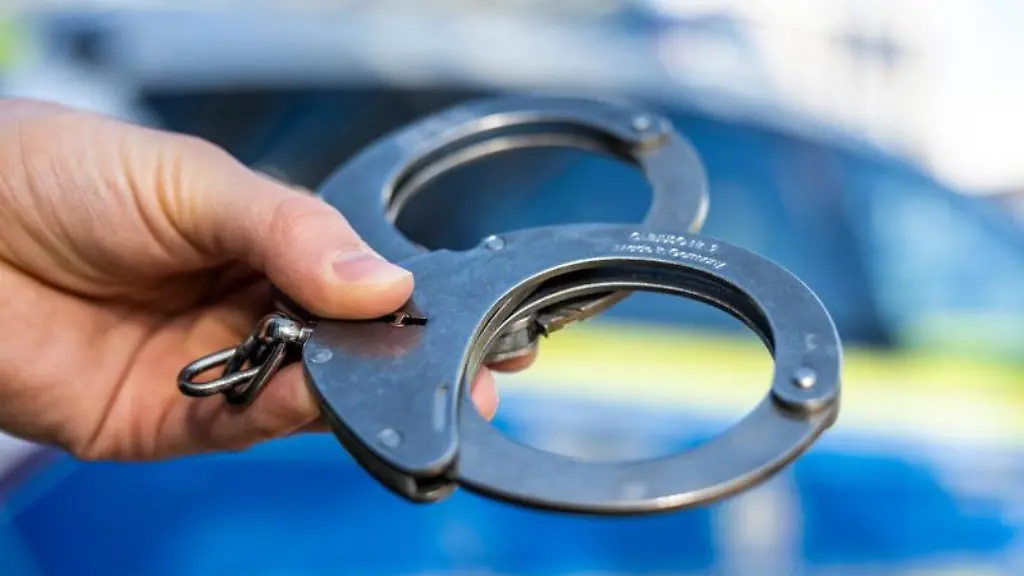 Eine-Hand-haelt-Handschellen-vor-einen-Streifenwagen-der-Polizei