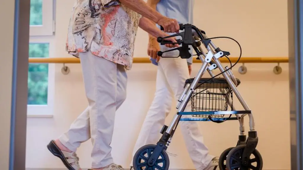 Eine-Pflegekraft-geht-in-einem-Pflegeheim-mit-einer-aelteren-Frau-ueber-einen-Korridor