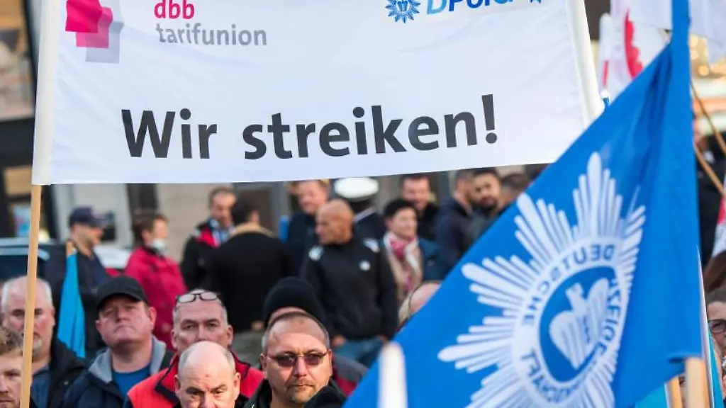 Teilnehmer-einer-Kundgebung-des-dbb-Beamtenbund-stehen-vor-der-Finanzbehoerde-und-halten-ein-Transparent-mit-der-Aufschrift-Wir-streiken-hoch