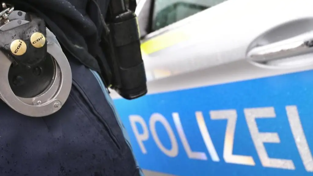 Ein-Polizist-mit-Handschellen-und-einer-Pistole-am-Guertel-steht-vor-einem-Streifenwagen