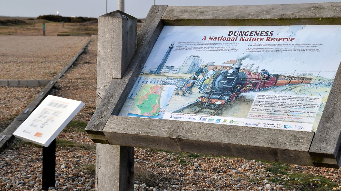 Neben einer der Informationstafeln zum National Nature Reserve und der Bahnlinie beim Atomkraftwerk Dungeness bei Kent steht ein Hinweisschild für einen Katastrophenfall des Atomkraftwerkes.