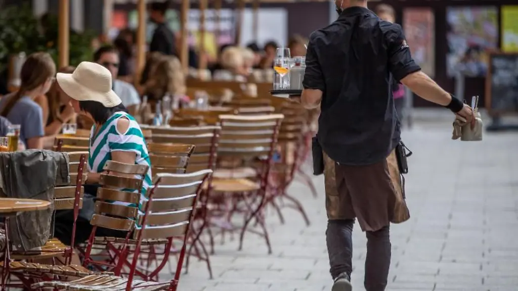 Eine-Servicekraft-laeuft-im-Aussenbereich-eines-Restaurants-an-Gaesten-vorbei