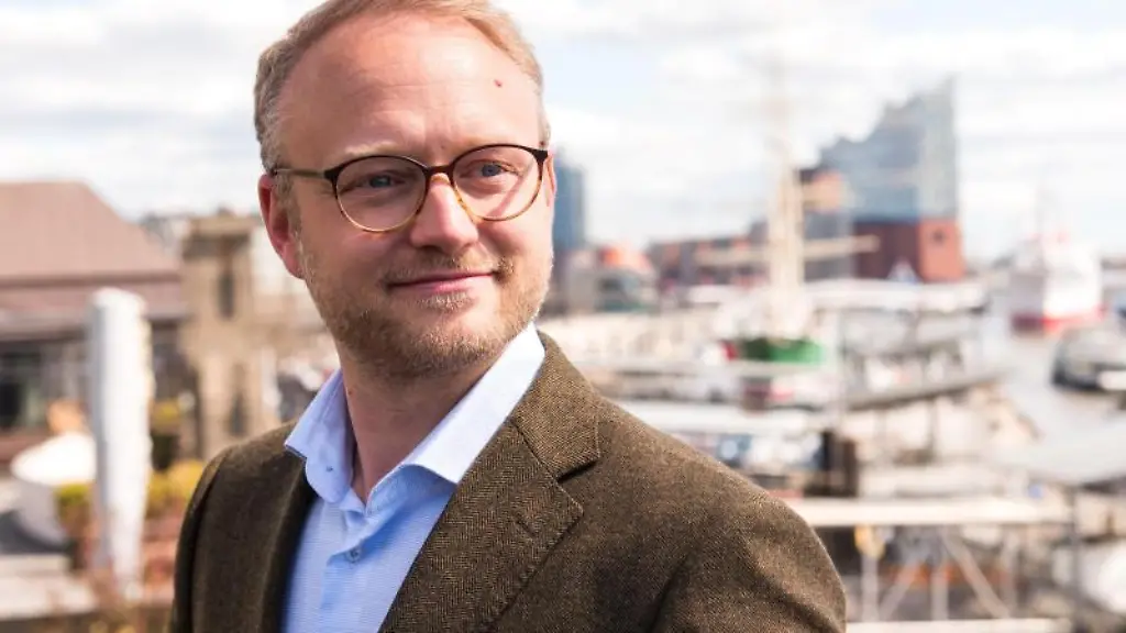 Michael-Kruse-laechelt-waehrend-eines-Online-Parteitags-vor-der-Kulisse-des-Hafens