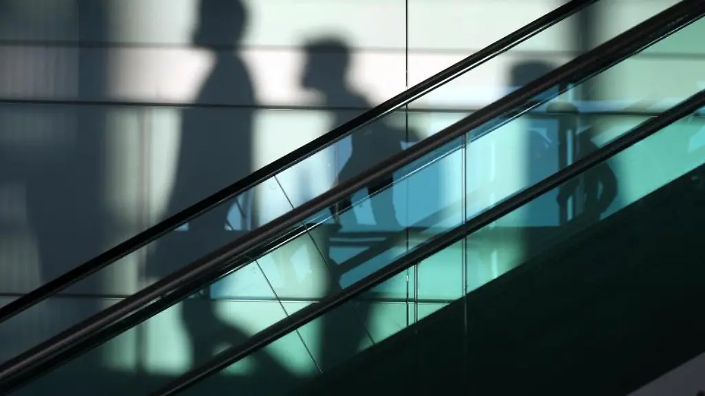 Die-Schatten-von-Reisenden-sind-auf-dem-Airport-Franz-Josef-Strauss-hinter-einer-Rolltreppe-zu-sehen