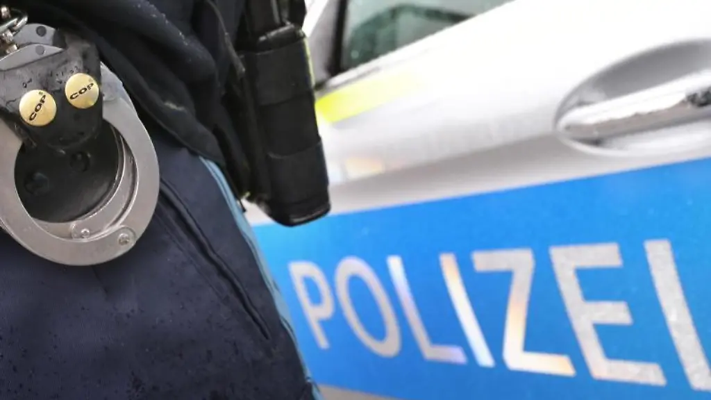 Ein-Polizist-mit-Handschellen-und-einer-Pistole-am-Guertel-steht-vor-einem-Streifenwagen